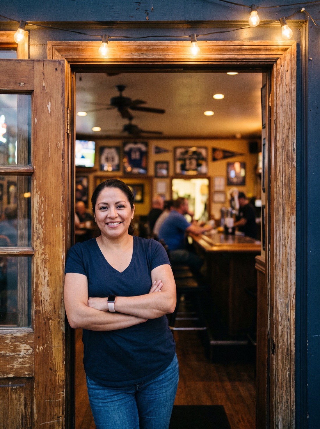 A bar owner standing in the doorway of her tavern at dusk.