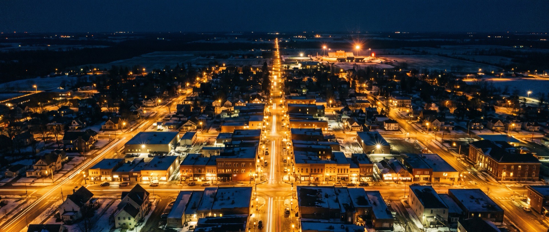 Aerial view of a small town's main street glowing at night.