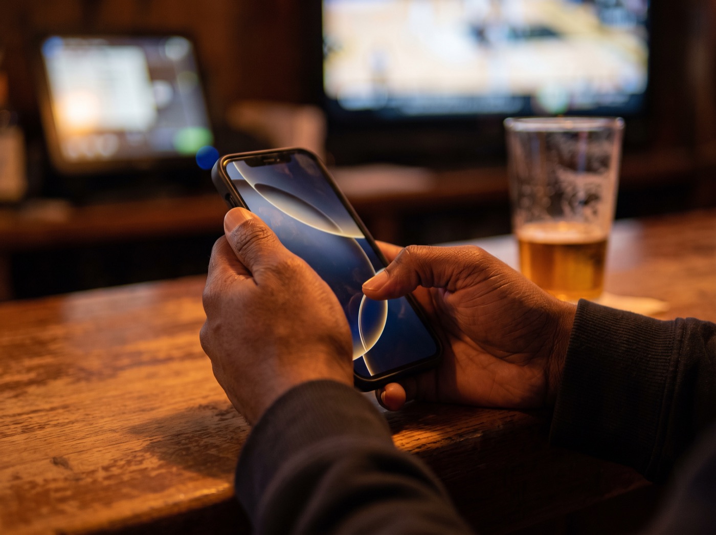Hands holding a phone at a bar counter.